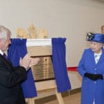 Queen Elizabeth II unveiling a brass commemorative plaque on a wooden easel.
