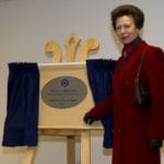HRH The Princess Royal standing beside a wooden easel with blue curtains, unveiling an oval plaque for the St Andrew's First Aid National Headquarters.